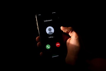 Hand holding mobile phone with unknown caller notification, concept of telephone fraud, call blocking, digital security, unwanted calls, anonymous communication, phishing attempt.