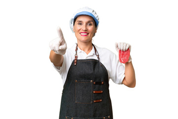 Butcher woman wearing an apron and serving fresh cut meat over isolated background showing and...