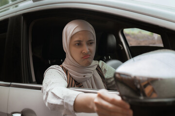 A woman is sitting inside a car, looking frustrated, while adjusting the side-view mirror. Perfect for illustrating emotions or driving-related themes.