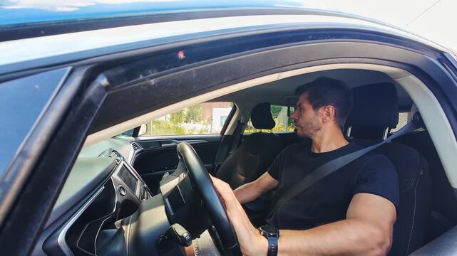 Male driver maneuvering car during parking, turning steering wheel and looking in mirrors. Person drives car, moves in reverse