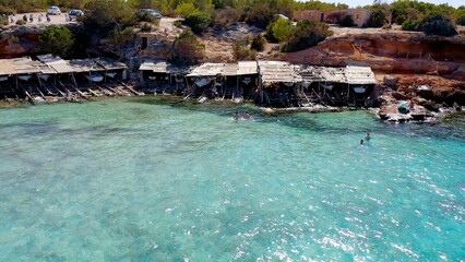 Aerial view of the small huts where the fishermen of Cala Saona keep their fishing boats, in...