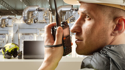 Industrial worker in hard hat communicates via walkie-talkie inside control room with machinery and...