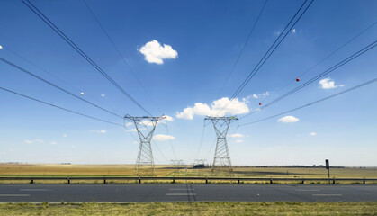 Power transmission towers over a flat South African landscape, clear blue sky and a highway