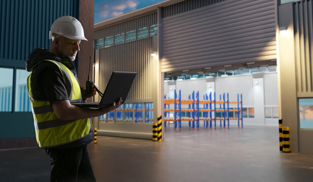 Man with laptop near warehouse hangar. Distribution center worker. Manager stands at gate to night warehouse. Logistician with computer ready to receive goods to warehouse. Man storekeeper in uniform