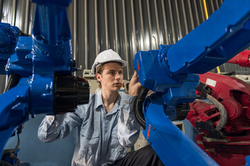 Engineer standing by robotic arm and operating machine in industry factory, technician worker check...