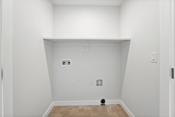 Small, empty laundry room with a white wall and a white shelf