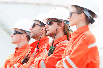 Oil refinery engineers team posing for photography in oil storage tank in background.