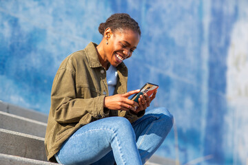 Smiling African young woman reading on phone in casual outfit