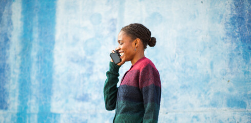 Young African woman smiling while talking on phone against blue wall