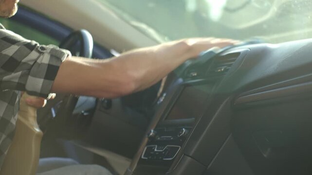 Man cleaning car dashboard with microfiber cloth and spray bottle. Concept of auto interior maintenance, vehicle disinfection and car hygiene