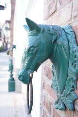 Close-up of antique green horse head hitching posts on a brick wall in a quiet urban street in...
