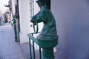 Close-up of antique green horse head hitching posts on a brick wall in a quiet urban street in...