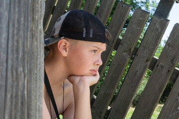  A young boy wearing a cap, resting his chin on his hand, concept of childhood reflection, summer...