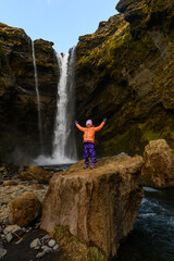 Small cute girl raising her arms up in front of Kvernufoss waterfall in Iceland