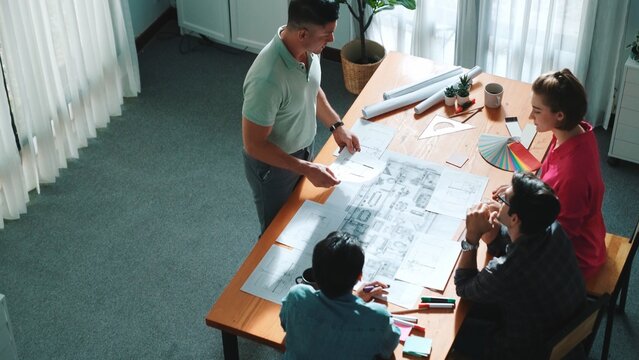 Top view of interior designer planing building while project manager working and holding coffee. Group of engineer brainstorming idea and designing house structure while presenting idea. Symposium.