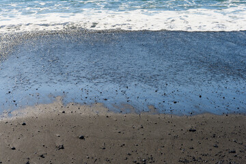 Small waves rolling up at Reynisfjara black sand beach in Iceland