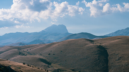 Rolling hills at the foot of Gran Sasso, Abruzzo, Italy, captured at sunset with warm golden light, soft shadows, and a serene landscape blending nature’s curves with mountain majesty.