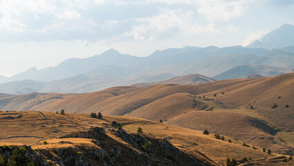 Rolling hills at the foot of Gran Sasso, Abruzzo, Italy, captured at sunset with warm golden light, soft shadows, and a serene landscape blending nature’s curves with mountain majesty.