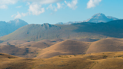Rolling hills at the foot of Gran Sasso, Abruzzo, Italy, captured at sunset with warm golden light, soft shadows, and a serene landscape blending nature’s curves with mountain majesty.