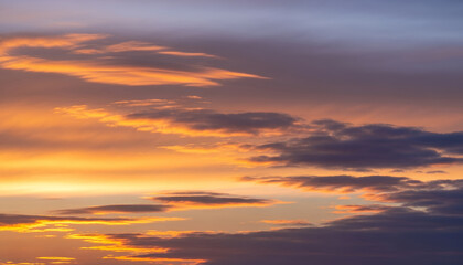 Fototapeta premium Soft orange light spreads across layered clouds at twilight, blending warm and cool tones in a peaceful skyscape that captures the beauty of evening light.
