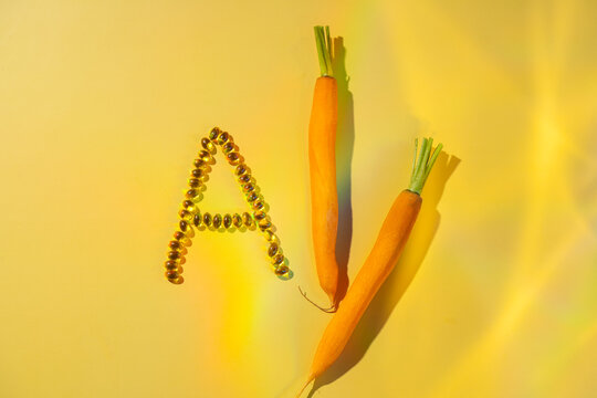 Vitamin A softgels with carrots on a yellow background
