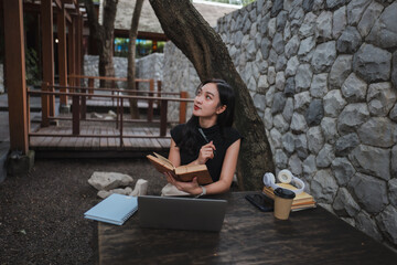 Young Asian Woman Thinking and Reading a Book Outdoors