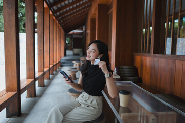 Young woman shopping online using credit card and smartphone in a cafe