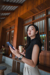 Young Asian businesswoman using smartphone and drinking coffee in a modern cafe