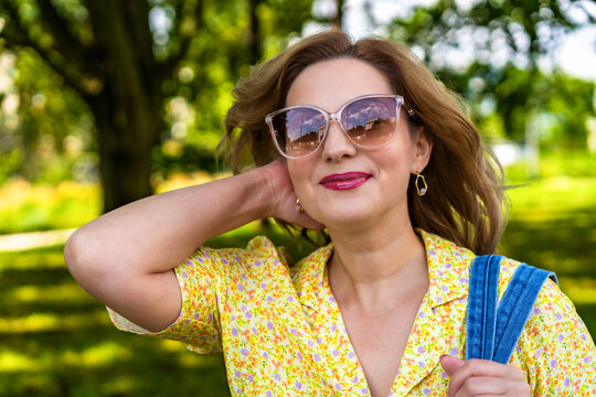 Portrait of beautiful smiling mature woman walking in city park on sunny summer day	 - Powered by Adobe