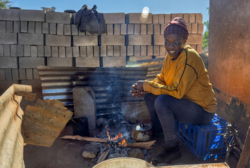 Africa village, single young woman sited in the summer outdoors kitchen by the fire cooking a meal