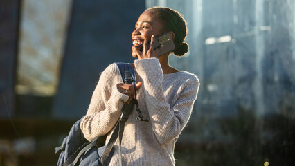 Laughing African American woman traveler on phone outdoors