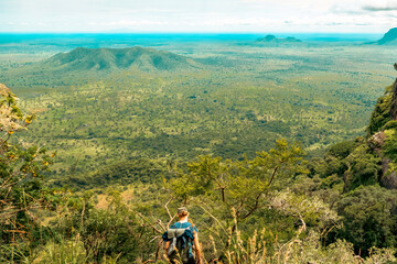 A hiker with a backpack against the background of Valley and mountains against sky at Mount Napak in Karamoja Region, Uganda 