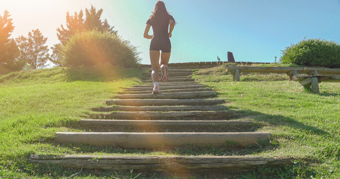 Female athlete running up a wooden staircase in a park during a sunny summer day
