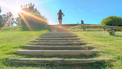 Rear view of a female athlete running up outdoor stairs in a park on a sunny day