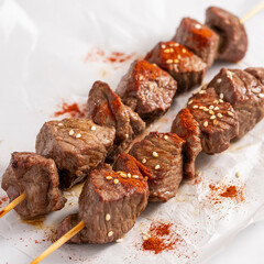 A close-up photograph of grilled beef kebabs on wooden skewers against a pure white background.