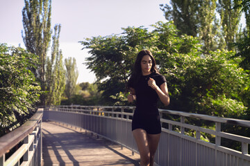 Concentrated sportswoman running on a wooden bridge in a park, enjoying her outdoor workout