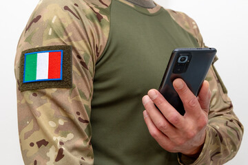 Fototapeta premium A man in military uniform with Italian flag patch holding a mobile phone.