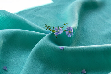 Blue flax flower and petals on teal linen fabric. Natural plant fiber for textile industry. Comfort, eco-friendliness of natural fabrics