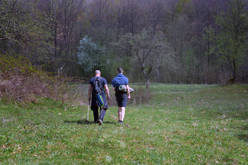 Back view of dad and son enjoying a spring walk in a wide green field near the forest. Perfect for...