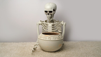 A laughing human skeleton holds a ceramic pot in his hands.