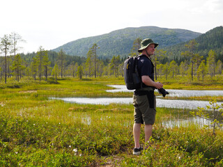Man with Camera Exploring a Beautiful Swampy Wilderness Area with Lush Greenery and Distant Forested Hills