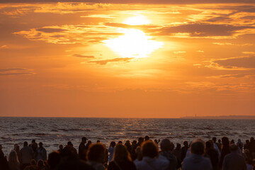People gather along the beach to witness the first red-orange glow of sunrise breaking through the...