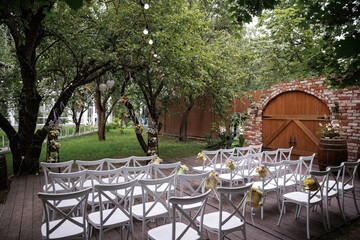Charming outdoor wedding ceremony setup featuring neatly arranged white chairs adorned with floral...