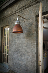 Rustic entrance with a door open into a charming brick building, featuring large copper pendant...