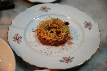 Exquisite gourmet dish presented on a decorated porcelain plate. Crispy potato strands and fresh...