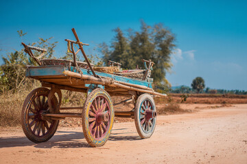 Obraz premium A majestic traditional ox cart (carreta) with painted wooden wheels, resting on a dusty rural road, symbolizing heritage.