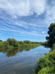 clouds over the river Beautiful summer landscape with a wide river and green trees along the banks. Blue sky with white fluffy clouds reflected.