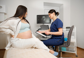 Female doctor showing prescription or notes on clipboard to pregnant woman during prenatal care...