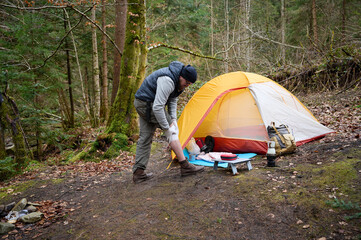 Hiker man with injured leg using first aid kit near the tent in the forest. A stressed trekker complaining alone in the mountain with broken knee.