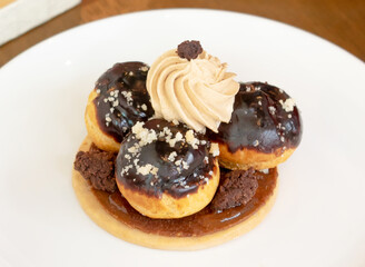 Gourmet Hazelnut Dark Chocolate Choux Cake topped with swirl of cream and crunchy nuts on White Plate closeup view of Elegant Dessert Pastry